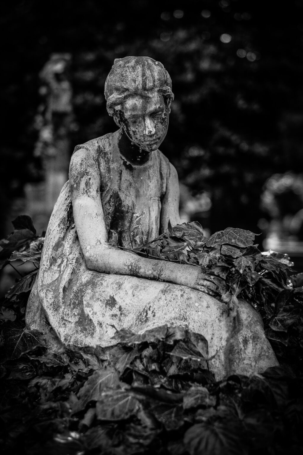 A vertical shot of a female statue  surrounded by leaves in black and white